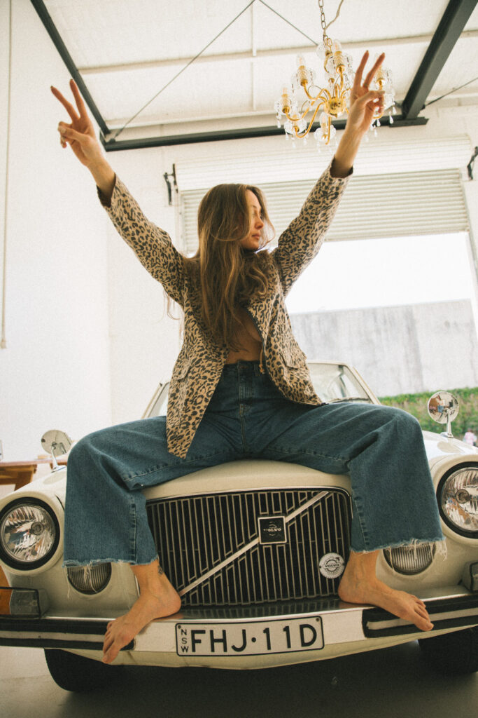 woman sitting on hood of classic care holding up peace fingers